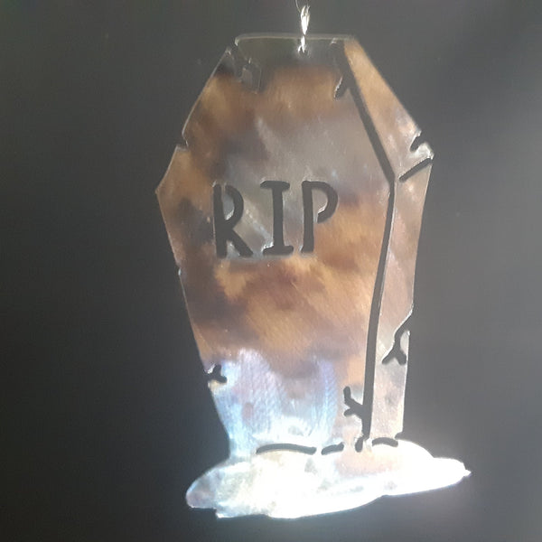 A coffin-shaped hanging ornament or plaque with 'RIP' engraved on it, glowing with warm amber light from within against a dark background.